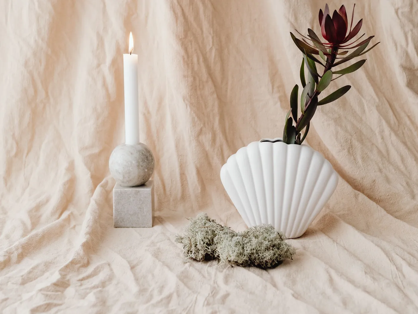 A lit white candle beside a white ceramic vase holding a small green plant